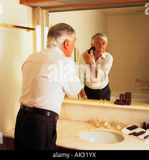 Man shaving with battery operated shaver in front of bathroom mirror. Stock Photo