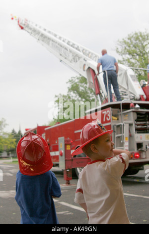 Two excited young boys watching a ladder being extended on a ladder truck at a safety fair Stock Photo