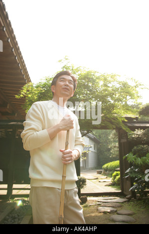 Mature man standing in the Front or Back Yard with a broom, low angle Stock Photo