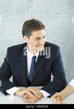 Businessman sitting at table, smiling at colleague Stock Photo