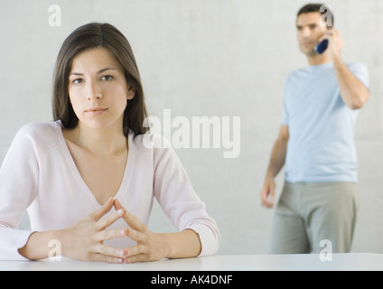Woman sitting, looking at camera while man uses cell phone in background Stock Photo