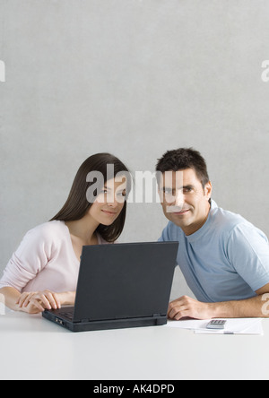 Couple using laptop, smiling at camera Stock Photo
