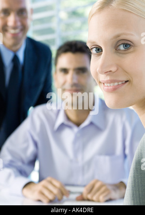 Businesswoman smiling at camera, colleagues in background Stock Photo