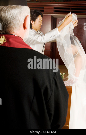 Groom lifting the bride's veil, with minister looking on Stock Photo