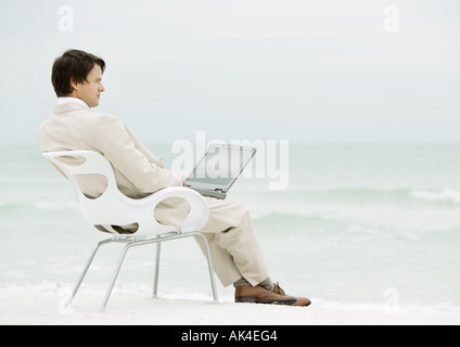 Businessman sitting in chair on beach, with laptop Stock Photo