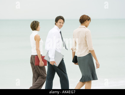 Business team walking on beach, businessman looking over shoulder at camera Stock Photo