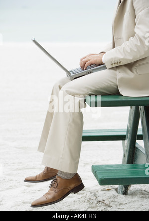 Businessman sitting on picnic table on beach, using laptop, chest down Stock Photo