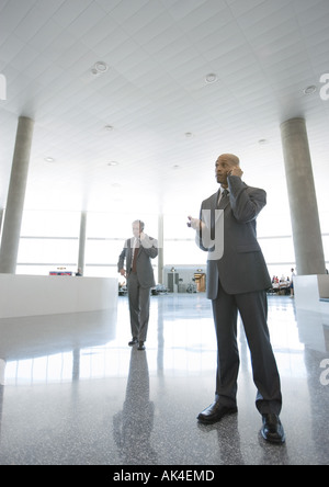 Businessmen using cell phones in airport concourse Stock Photo