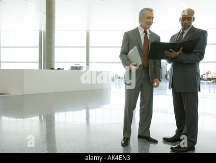 Two businessmen standing in airport concourse, looking at agenda Stock Photo