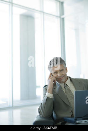 Businessman using cell phone and laptop in lobby Stock Photo