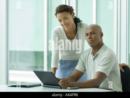 Businessman sitting at desk while woman leans over shoulder, smiling at camera Stock Photo