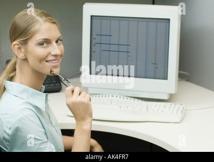 Female office worker sitting at computer, smiling at camera Stock Photo