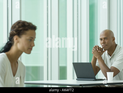 Man sitting with laptop, looking at female co-worker Stock Photo