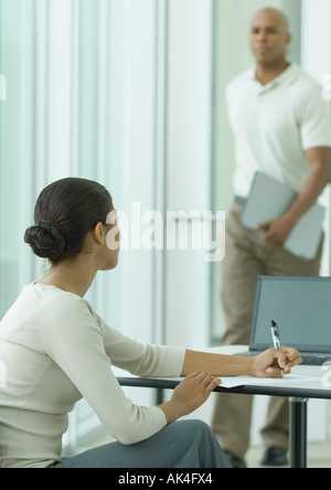 Female office worker looking up as man enters Stock Photo