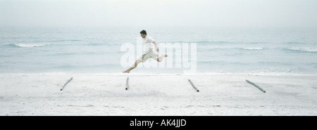 Man jumping over logs on beach, side view Stock Photo