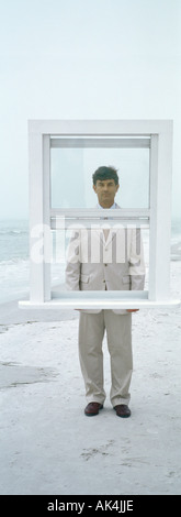 Businessman standing behind window frame on beach Stock Photo