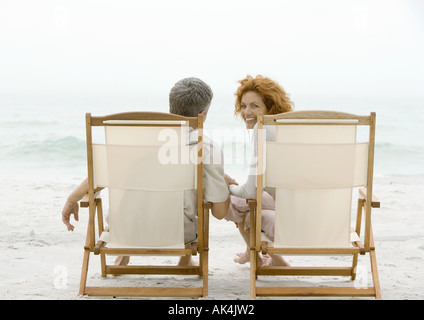 Couple sitting in beach chairs, woman turning around, looking at camera Stock Photo