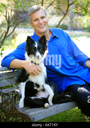 A handsome man relaxes with a border collie dog in a garden setting Stock Photo