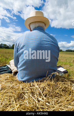 Lone figure sitting on a pile of straw in a field Stock Photo