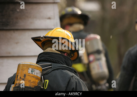 Three firefighters geared up at a house fire that has been extinguished Stock Photo