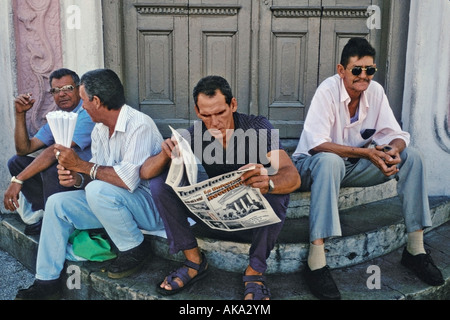 Four men on sitting on doorsteps on a street corner in Santiago de Cuba Stock Photo