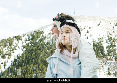 Two young skiers standing together, looking away, one's arm around the other's shoulder Stock Photo