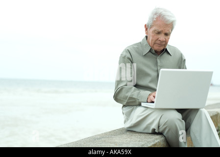 Senior man sitting outdoors, using laptop computer, looking down Stock Photo