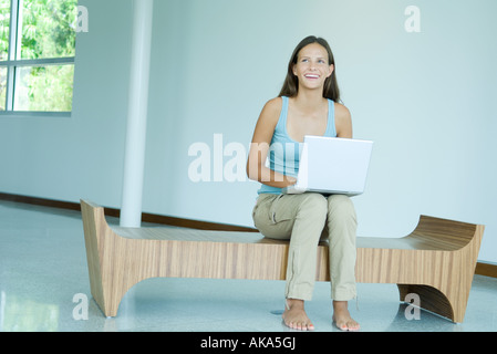 Teen girl sitting on bench, using laptop computer, smiling, looking up Stock Photo