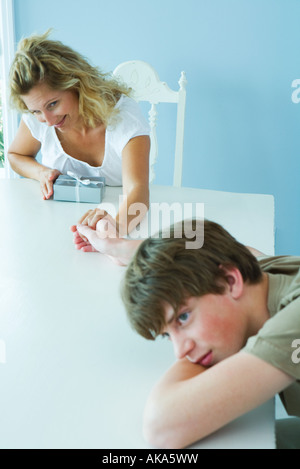 Woman with present holding hands with teen boy who is resting head on arms and looking away Stock Photo