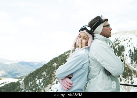 Two young skiers standing back to back, smiling, one looking at camera, portrait Stock Photo