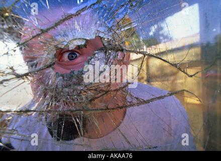 Man looking through broken glass window Stock Photo