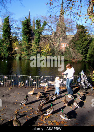 A young mother and her little boy feed the ducks at the Minster Pool in Lichfield Staffordshire England Stock Photo