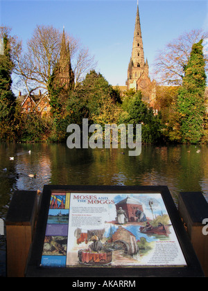 Lichfield Cathedral seen across Minster Pool with reflections Lichfield Staffordshire In the foreground is an information board Stock Photo