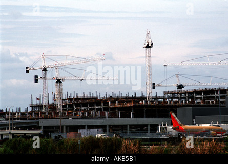 Tower cranes rise above a parking garage construction project of an airport against a blue sky  Stock Photo