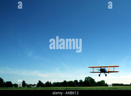 A colorful double winged aircraft flies in low for its landing atop a trim green field in day light Stock Photo