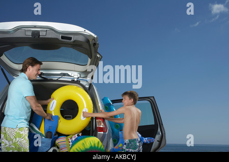 Father and son (10-12) unloading car full of beach accessories Stock Photo