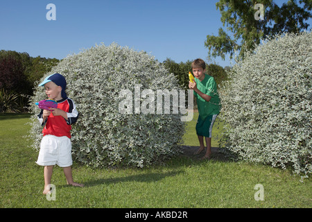 Two boys (3-11) playing with water pistols among bushes Stock Photo