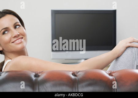 Young woman on sofa in front of flat screen television Stock Photo
