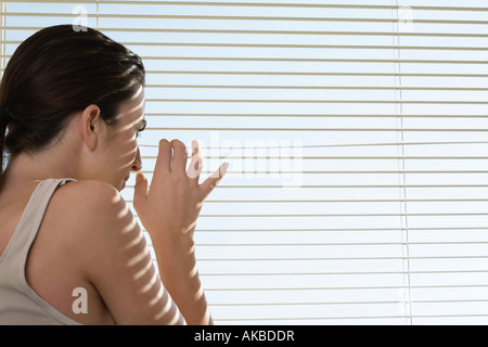 Young woman peering through blinds Stock Photo