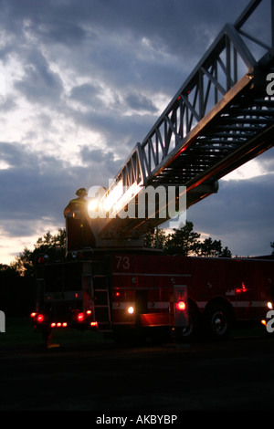 Two firefighters at the controls of the ladder of a fire truck at sunset Stock Photo