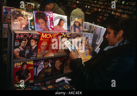 A female British Asian Bollywood movie fan avidly reads magazines from rack in a bookshop in Southall London Stock Photo