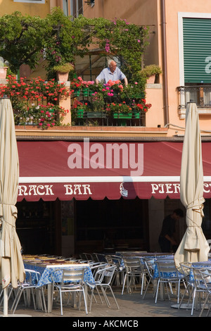 Elderly man stands on apartment deck above a ground floor restaurant looking out over Campo S Mahgerita in Venice Italy Stock Photo