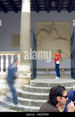 South-East Europe, Croatia, Dalmatia, Trogir, tourist on stone steps photographing metal gate in front of carving Stock Photo