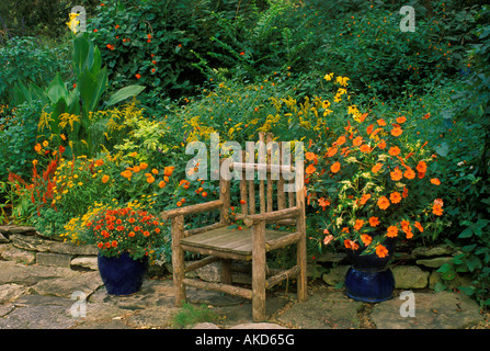 Hand made wooden chair on rock patio by garden with orange and flowers and blue  ceramic flowerpots Stock Photo