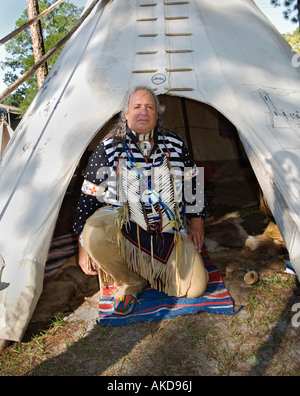 Native American reenactor, Ken Miller, aka Cross Eagle, kneels at entrance to his tepee lodge at Native American festival in Lake City,, Florida. Stock Photo