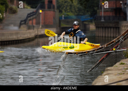 Kayaker in his yellow playboat sliding off a ramp into the river Foss in York. UK Stock Photo