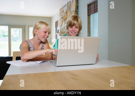 Sister and brother (8-11) sitting at table, using laptop, smiling Stock Photo