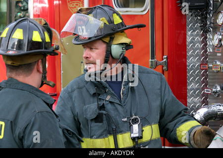 Two fire fighters talking at a fire emergency scene to supply water from the pumper to the firefighters working the scene Stock Photo