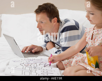 Father and daughter drawing and using laptop on bed Stock Photo