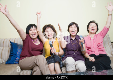 Three senior women and a mature woman singing in front of microphones with their hands raised Stock Photo